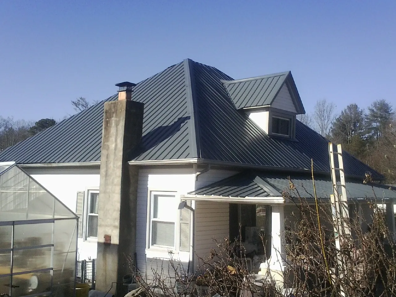 Dark blue standing seam metal roof on a white farmhouse with dormer — Slate & Tile Roof Repair by Roofing Brothers in Casper