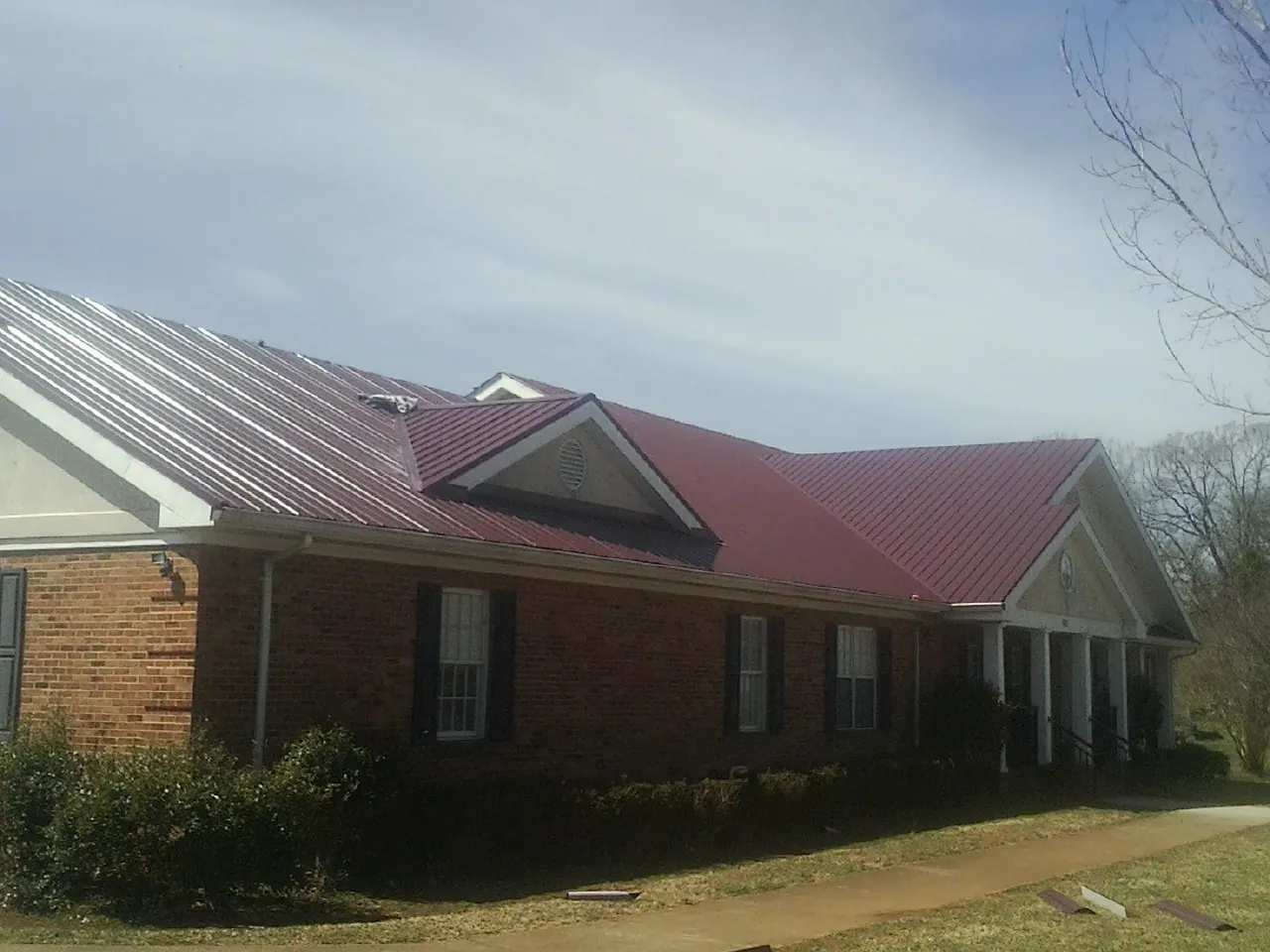 Red metal roof with gabled entries on a long brick building, from a Hail Damage Roof Repair job in Casper