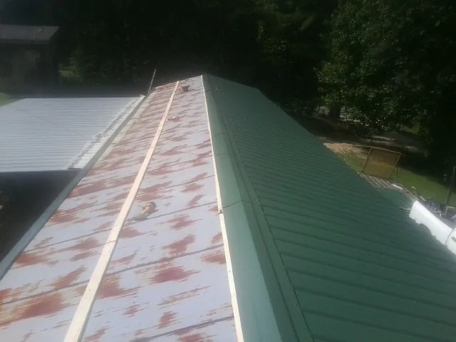 Old rusted panels beside newly installed green metal roofing — Wind Damage Roof Repair by Roofing Brothers in Casper